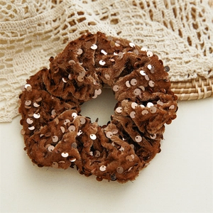 Close-up of brown velvet hair scrunchie with sparkling bronze sequins on lace background