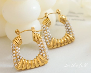 Macro detail of gold-toned C-shaped earrings with spiral texture and mini pearls