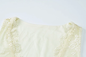 Detail of elegant V-neck lace trim on a cream summer dress with delicate floral embroidery