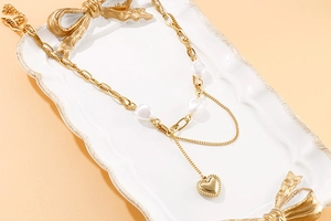 Gros plan détaillé du pendentif cœur doré et des perles baroques sur un collier étagé