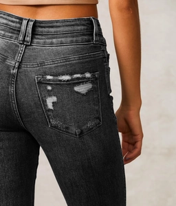 Detail of distressed back pocket on washed black vintage denim jeans with frayed edges