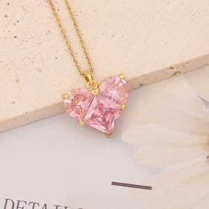 Pink heart crystal pendant on golden chain necklace over a textured stone background