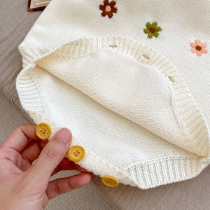 Détail de barboteuse en tricot pour bébé avec broderies fleurs et boutons en bois