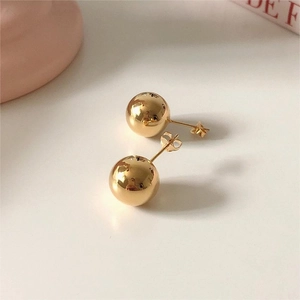 Macro detail of glossy golden spherical stud earrings with minimalist polished surface