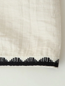 Detailed macro view of beige linen fabric with black embroidered geometric pattern edges
