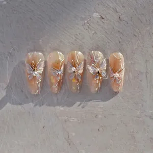 Detailed view of amber gradient press-on nails with 3D butterfly, pearls, and gold foil