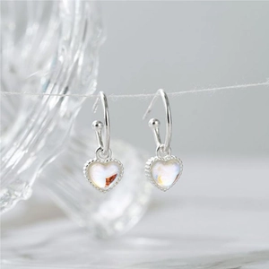 Macro detail of heart-shaped silver earrings with rainbow stones on a marble background
