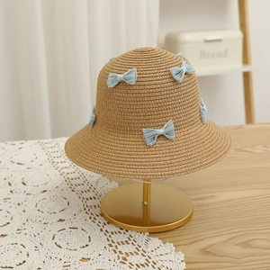 Detail of hand-woven straw hat with light blue lace bows on a gold display stand