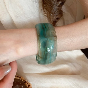 Detailed view of a wide acrylic bangle with green and blue marble texture on a wrist