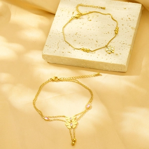 Close-up of golden clover bracelet with white shell and pink butterfly charm on silk background