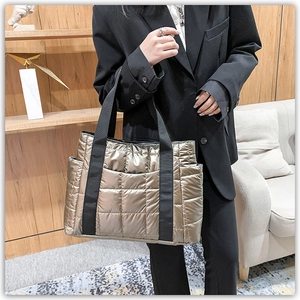 Close-up of quilted gold puffer tote bag with metallic finish and black woven straps
