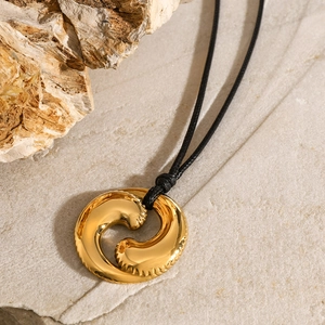 Detail eines goldenen Wellenanhängers mit schwarzer Kordel auf einem natürlichen Stein