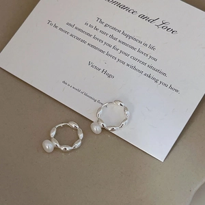 Close-up of 925 sterling silver pearl earrings with twisted rope texture on a warm background