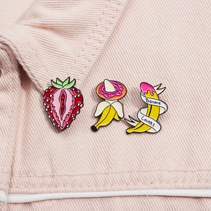 Macro detail of strawberry and banana enamel pins on pink denim fabric background