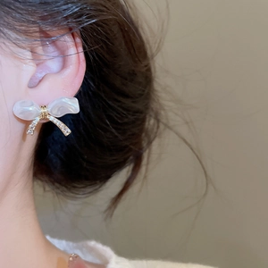 Close-up of elegant bow earrings with pearls and sparkling zircons on a model