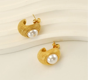 Détail de boucles d'oreilles dorées en C avec texture tressée et perle blanche au centre
