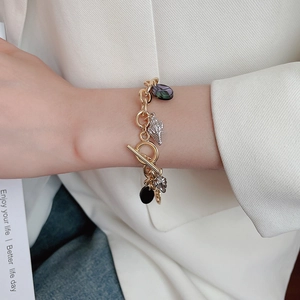 Detail of gold ocean charm bracelet with shell pendants and OT toggle clasp on wrist