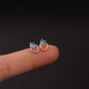 Macro shot of silver and gold heart stud earrings with blue zircons on fingertips