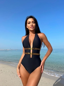 Detail of black one-piece swimsuit with halter neck and gold waist hardware on beach