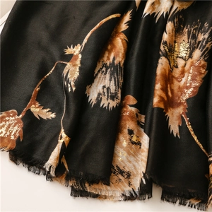 Close-up of black cotton-linen scarf featuring gold floral patterns and fringe details