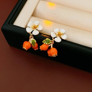 Detail view of vintage enamel flower earrings with orange berry charms on a black tray