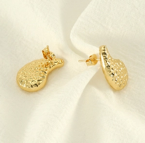 Detailed view of gold hammered texture teardrop stud earrings on soft fabric