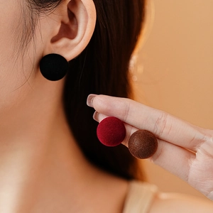 Detail of round flocked velvet stud earrings in black, burgundy and brown colors