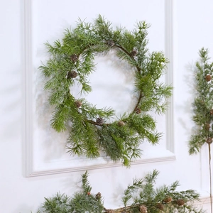 Artificial Christmas wreath with green pine needles and pine cones on a white wall