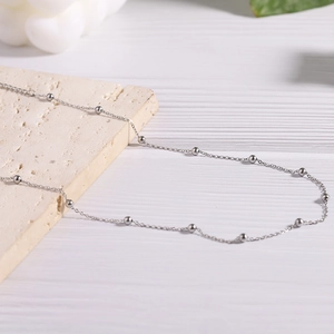 Detail shot of a silver minimalist stainless steel bead chain on a textured stone surface