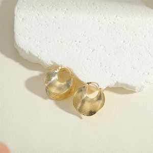 Elegant geometric gold swirl earrings with shell design on white stone background