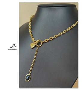 Detail of gold heart necklace with black oval pendant and OT toggle on stainless steel chain
