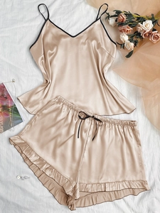 Detail of champagne satin camisole set with V-neckline and ruffled shorts on white fabric