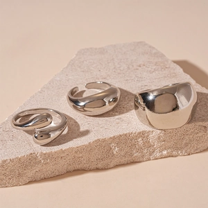 Detailed view of three minimalist silver-finish geometric rings on a stone display
