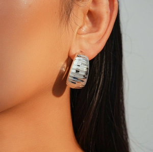 Macro shot of silver C-shaped wide hoop earring with textured metallic surface on model