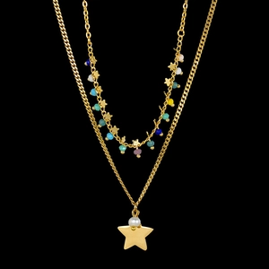 Detail of double-layer gold necklace with colorful beads, stars and pearl on black background