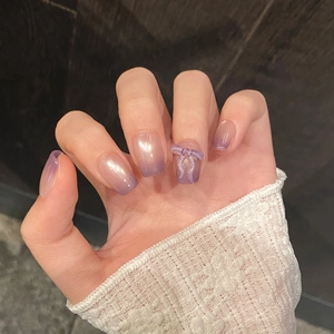 Detail of gradient purple press-on nails featuring cat eye finish and a 3D bow accent