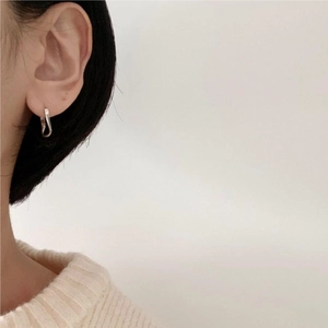 Close-up of minimalist silver curved hoop earrings worn by a model in a knit sweater