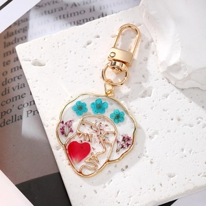 Artistic resin face keychain with colorful dried flowers on a white stone background