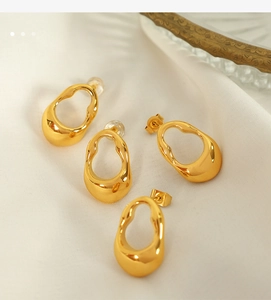 Macro shot of minimalist irregular oval gold earrings on elegant white satin fabric
