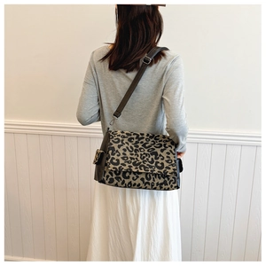 Detail view of leopard print crossbody bag with black leather straps and flap closure