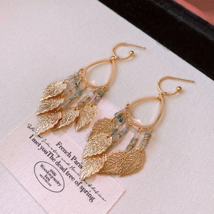 Detail of vintage gold tassel earrings with green beads and delicate leaf pendants