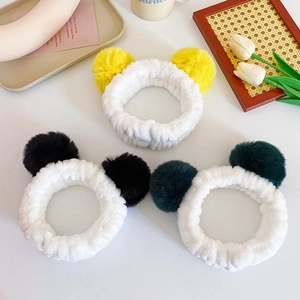 Three soft plush hairbands with colorful pom poms on a cozy white desktop setting
