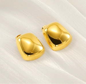 Close-up of polished gold rectangular stud earrings on white silk background