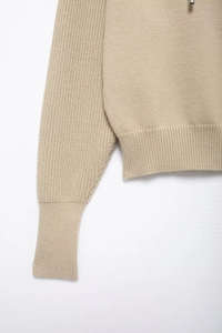 Detail of beige knitted hoodie showing ribbed cuffs and premium metal drawstring tips