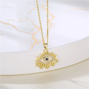 Close-up of golden Evil Eye necklace with clear zircons and blue stone on marble plate