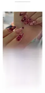 Detail of burgundy and nude almond press on nails with marble patterns and gold beads