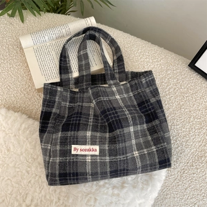 Detailed view of the gray plaid tote bag texture and white woven brand label on surface