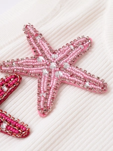 Macro shot of pink starfish charm with silver beads and rhinestones on knit fabric