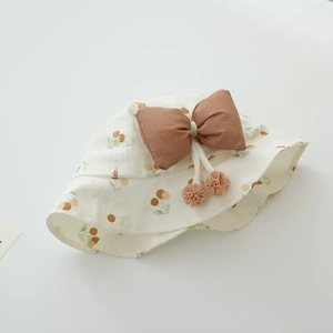 Close-up of cream baby sun hat with cherry print, large brown bow and pink pom-poms