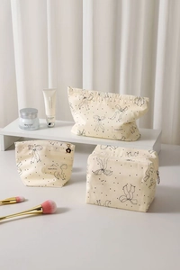 Detailed set of three beige cosmetic bags featuring black bow patterns and metal zippers